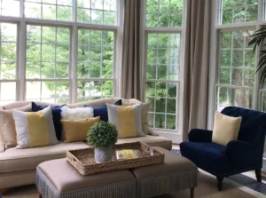 Bright living room with large windows, beige sofa, blue armchair, and wicker accents